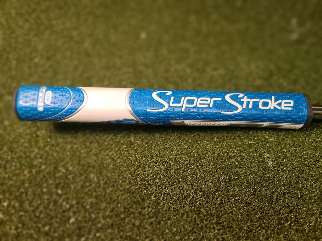 A blue and white golf putter head labeled 'Super Stroke' resting horizontally on a green turf-like surface.