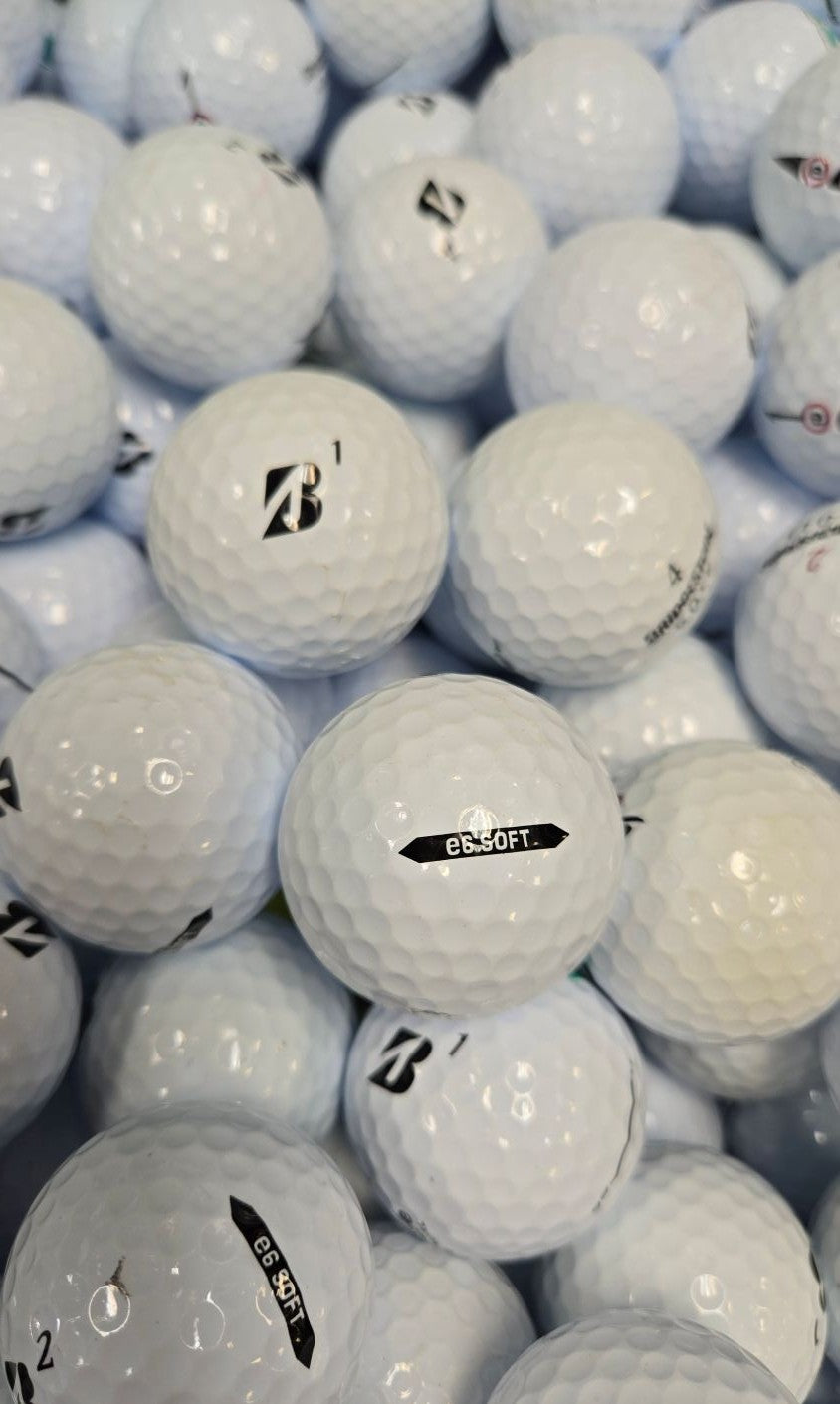 A close-up pile of white golf balls, including a central Bridgestone golf ball with a black 'B' logo and another with a black 'E6 SOFT' label.