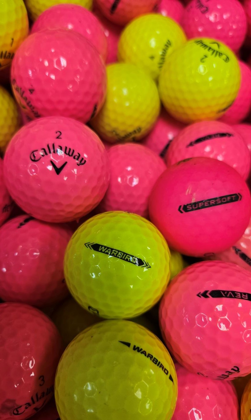 A close-up pile of golf balls in bright neon pink and fluorescent yellow-green, with visible Callaway and Supersoft branding on several balls.