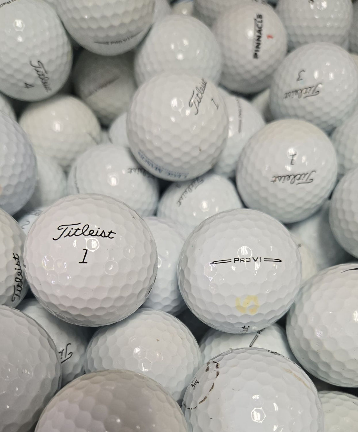 A pile of white Titleist golf balls, including a prominent Titleist Pro V1 ball in the foreground and several other balls with visible brand markings.