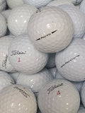 A close-up pile of white Titleist golf balls, with the top ball printed with 'Titleist PRO VIX' and other balls showing red numbers like 1, 2, 3, and 4.