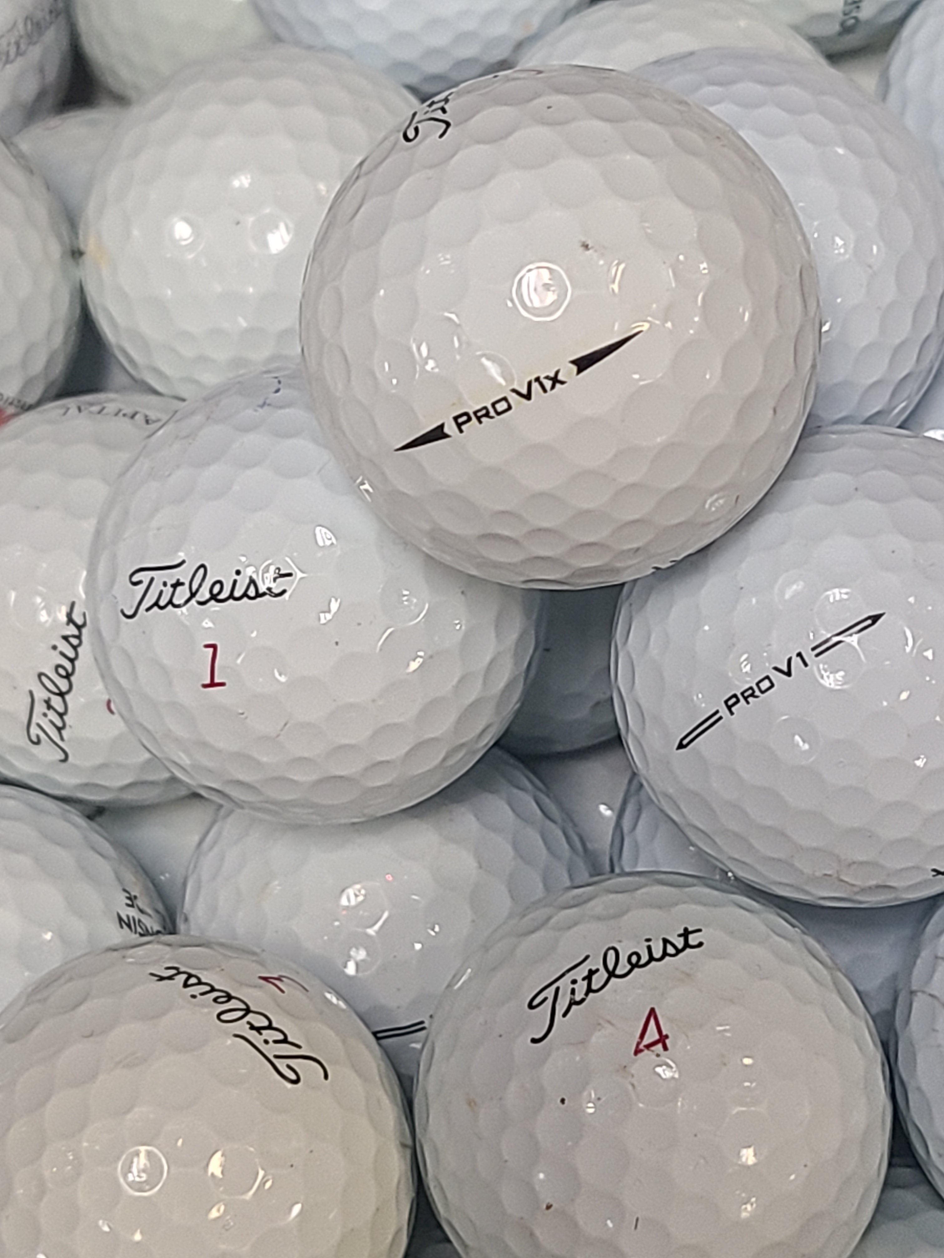 A close-up pile of white Titleist golf balls, with the top ball printed with 'Titleist PRO VIX' and other balls showing red numbers like 1, 2, 3, and 4.